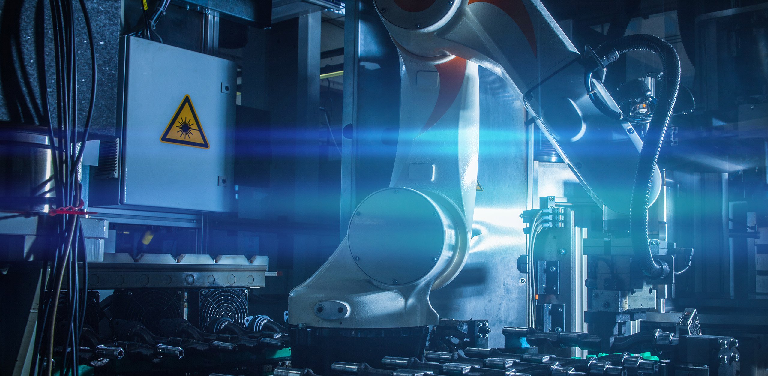Ein weißer Roboterarm führt präzise Laserbearbeitung an einem Werkstück durch; Technologie von MFT GmbH.